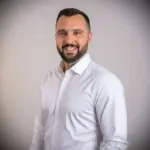 Professional agent with short dark hair and beard in white shirt, representing prime Ekosphere Ulcinj properties on immobilien.ekosphere.me.