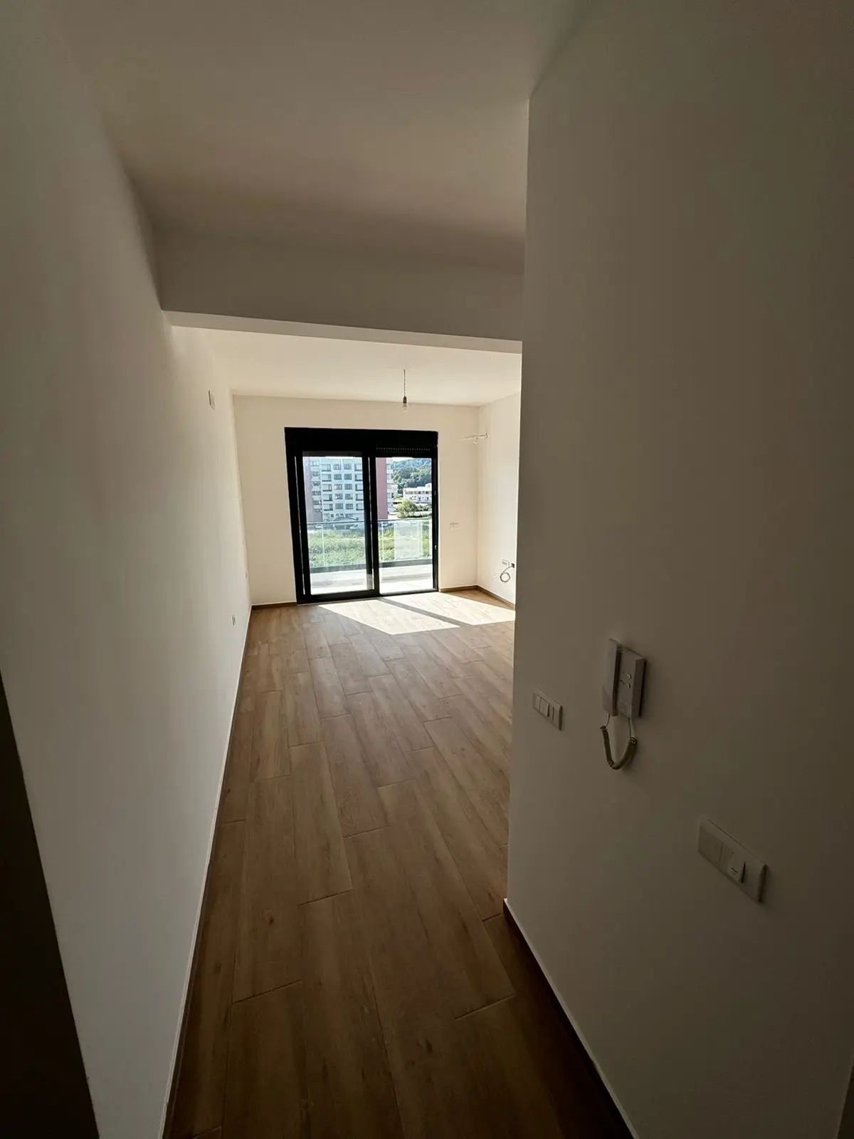 Modern empty room with white walls, wood floors, balcony and panoramic Ulcinj views&mdash;exclusive listing on immobilien.ekosphere.me by ekosphere doo.