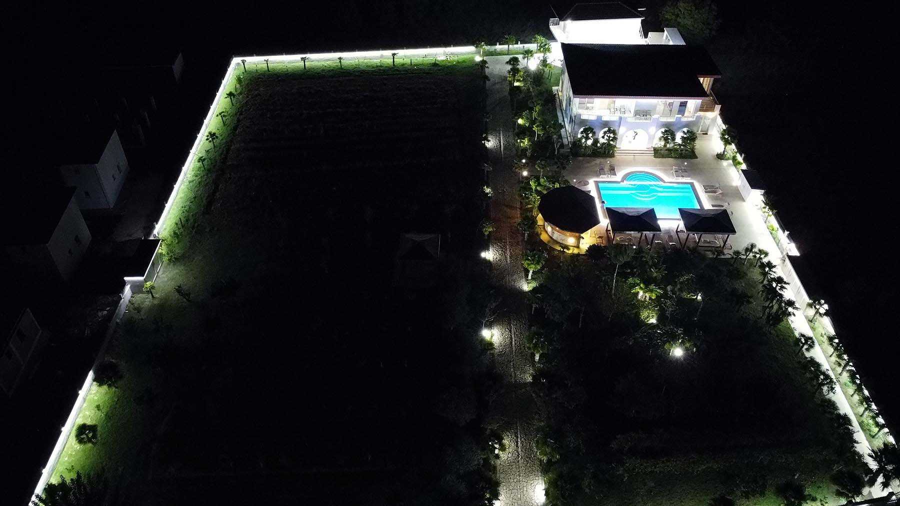 Stunning aerial night view: luxury modern home with pool, lush gardens, and illuminated fencing in Ulcinj Montenegro. An exclusive immobilien.ekosphere.me by ekosphere doo property investment opportunity.