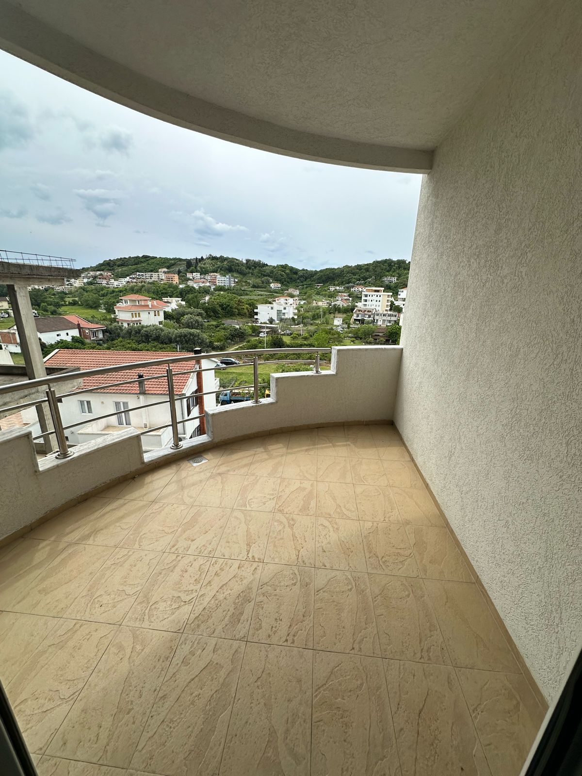 Spacious covered balcony with beige tiles and glass railing, boasting panoramic Ulcinj views&mdash;exclusive to immobilien.ekosphere.me by Ekosphere.