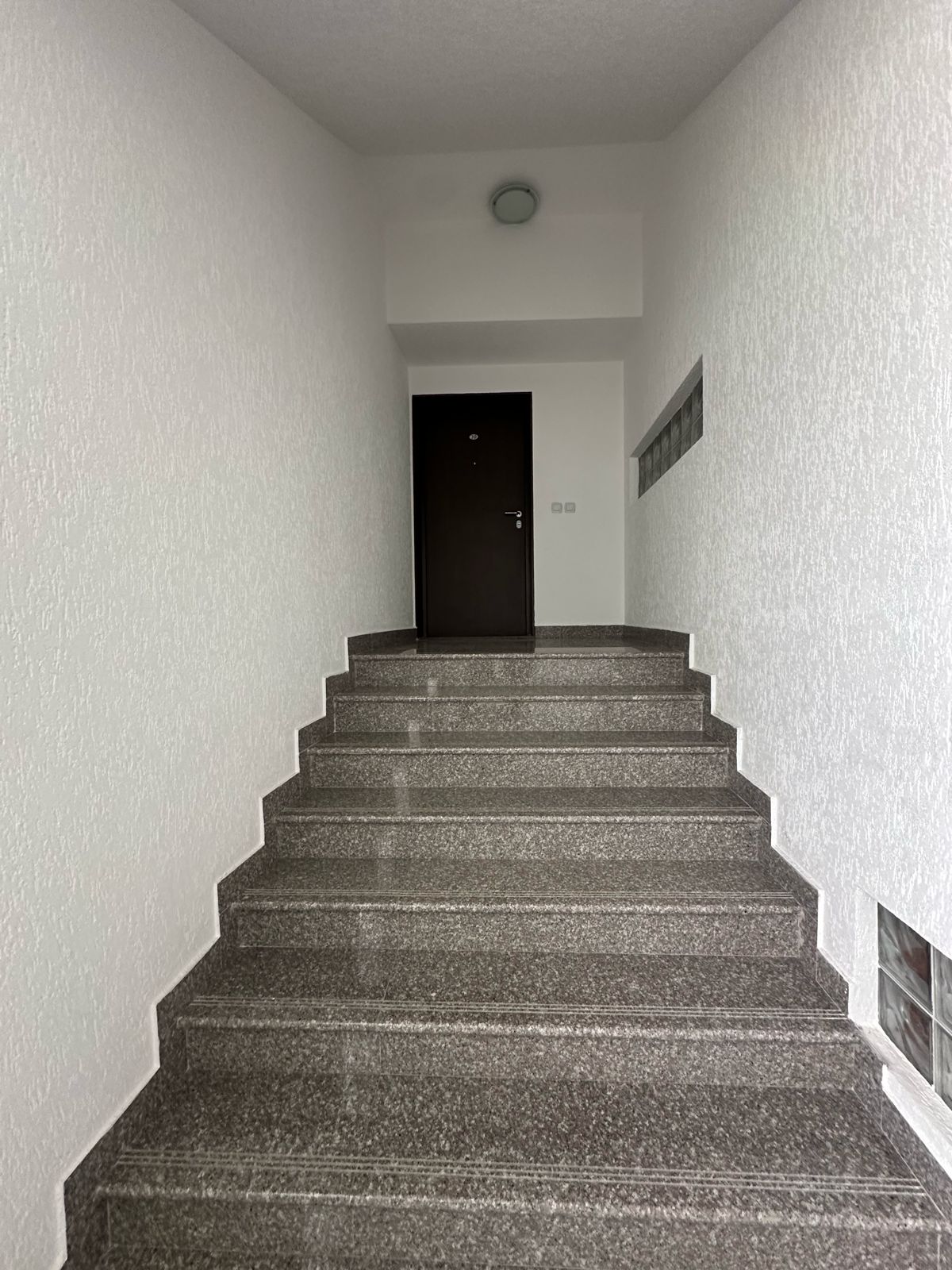 Modern staircase with sleek dark gray steps and glass block windows, ideal Ulcinj investment. Listed on immobilien.ekosphere.me by ekosphere doo.