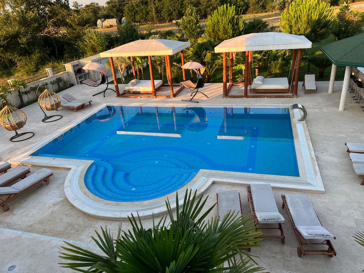 Luxurious pool oasis with blue tiles, lounge chairs, cabanas & chic seating&mdash;prime Ulcinj investment. Listed on immobilien.ekosphere.me.