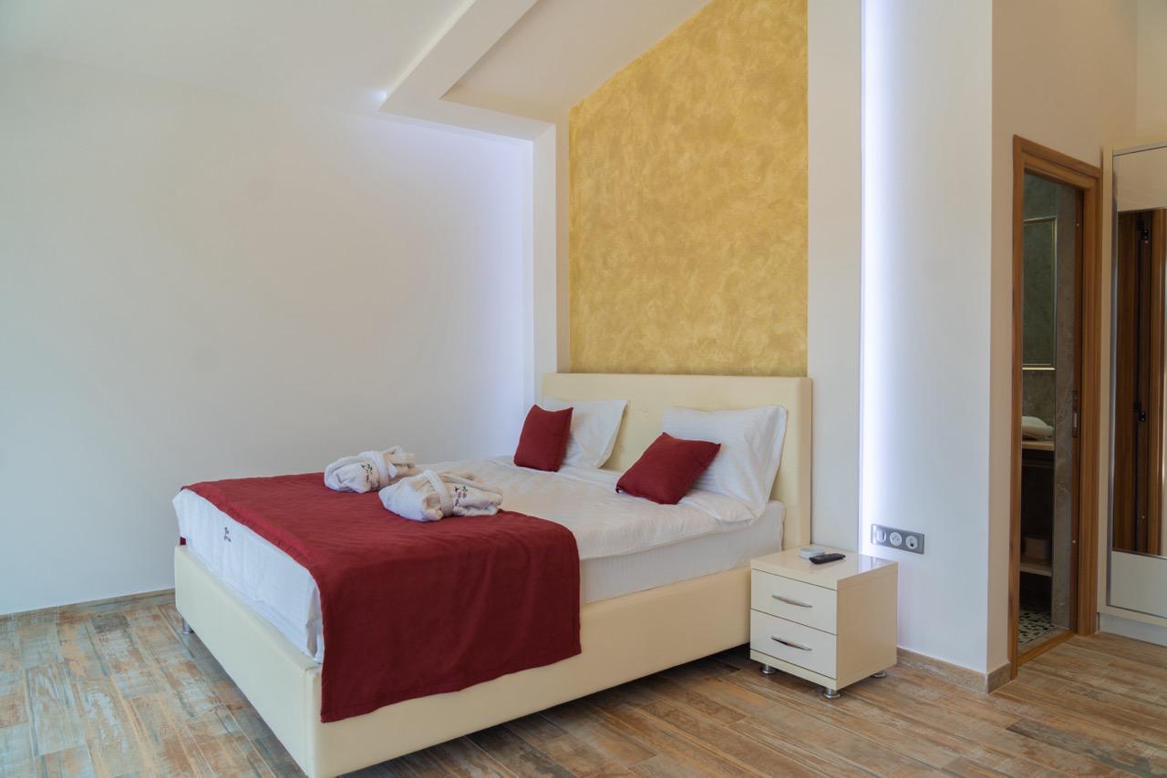 Elegant modern bedroom in Ekosphere, Ulcinj&mdash;double bed, white linens, red throw, wood floors. Invest via immobilien.ekosphere.me by ekosphere doo.