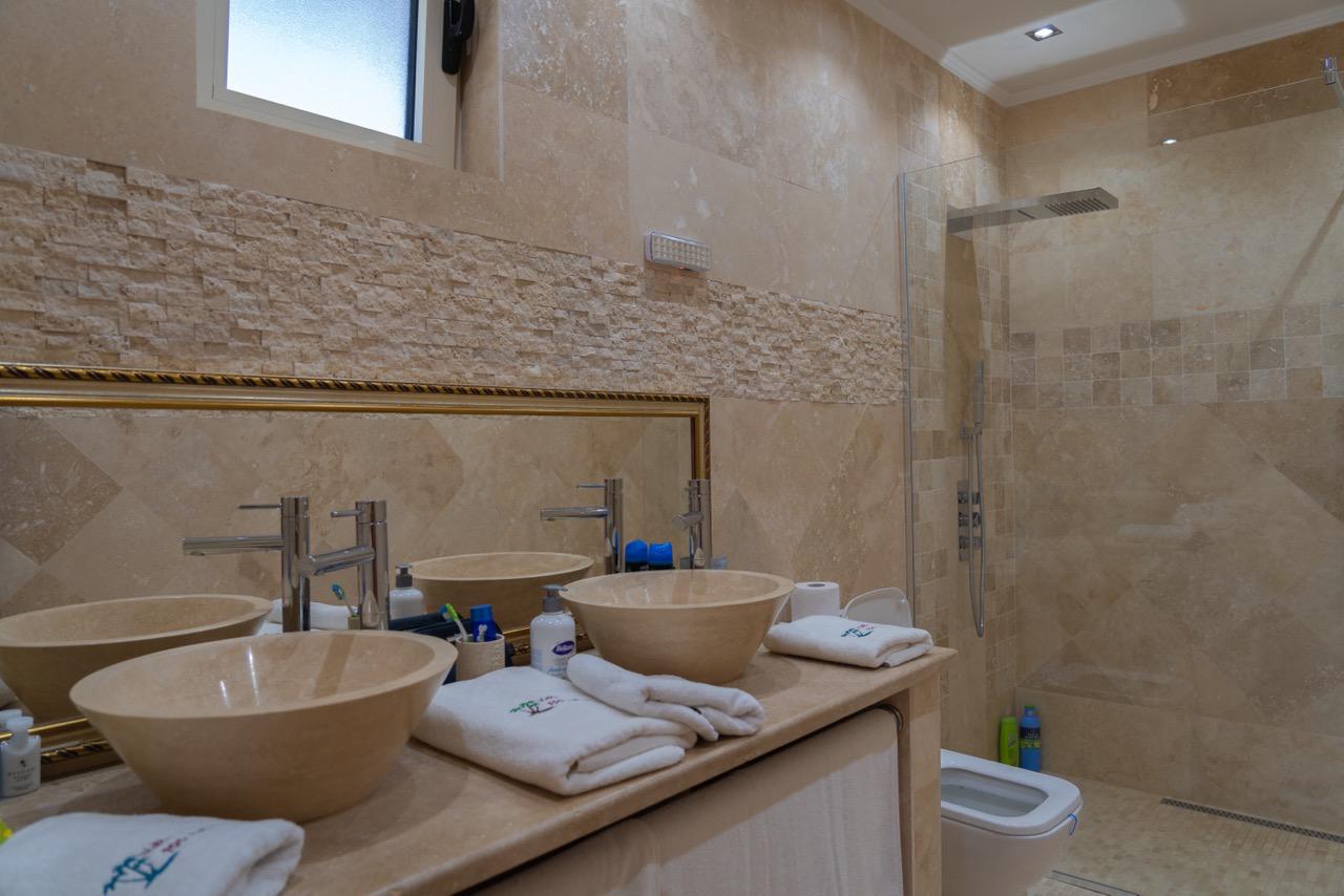 Luxury bathroom in Ulcinj, Montenegro: beige stone, double sinks, walk-in glass shower&mdash;exclusive Ekosphere/ immobilien.ekosphere.me property.