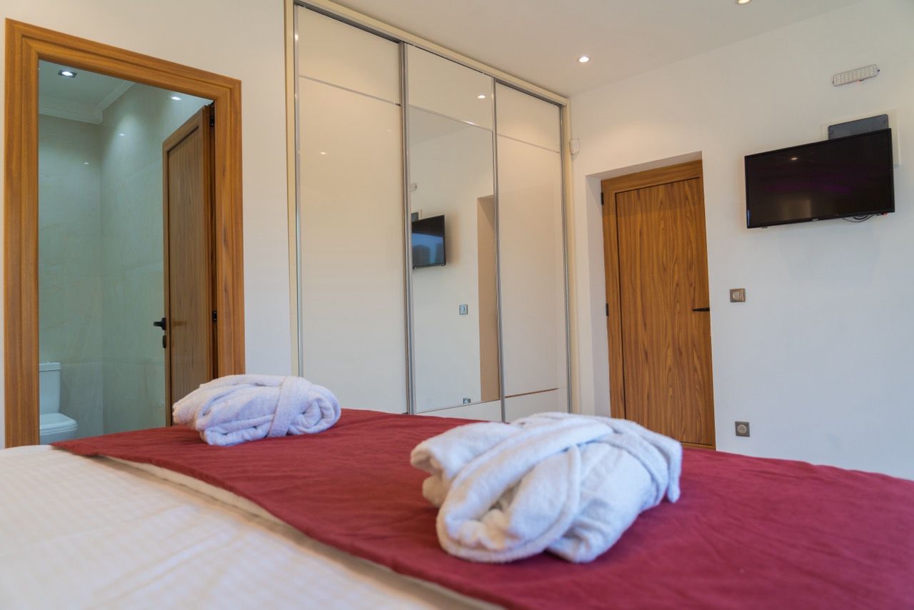 Modern Ulcinj property: elegant bedroom with red coverlet, bathrobes, premium finishes. Exclusive on immobilien.ekosphere.me by Ekosphere DOO.