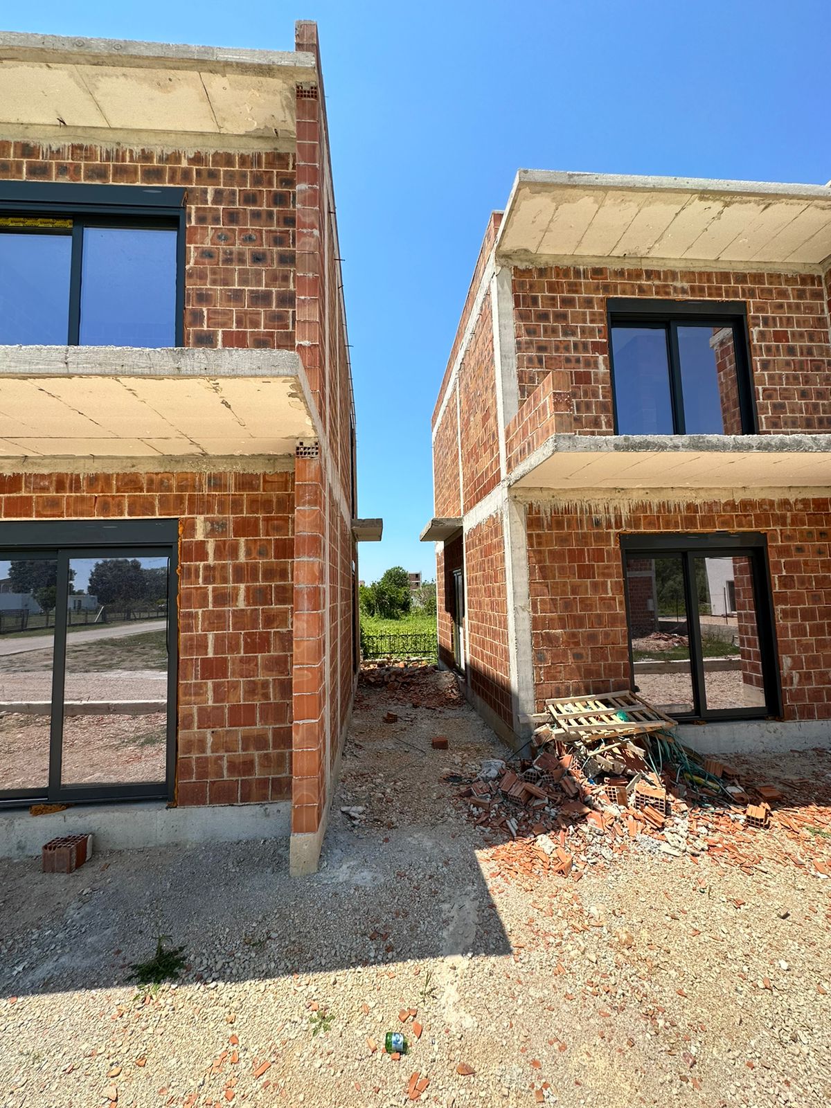 Prime Ulcinj investment: two unfinished brick homes with glass features, ideal for custom development. Listed by Ekosphere on immobilien.ekosphere.me.