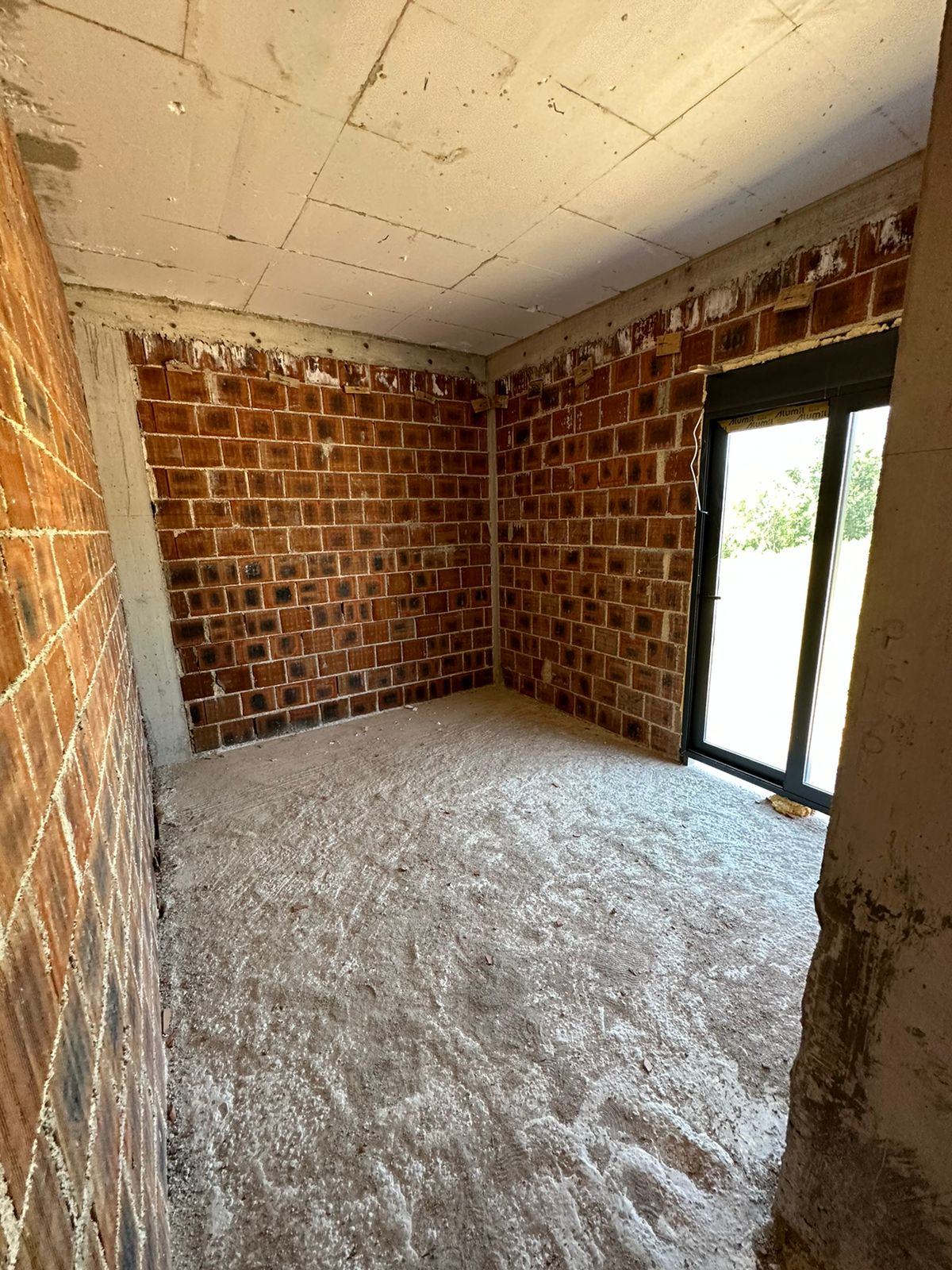 Spacious unfinished room in Ulcinj with red brick walls, concrete floor, large glass doors&mdash;prime investment at immobilien.ekosphere.me by ekosphere doo.