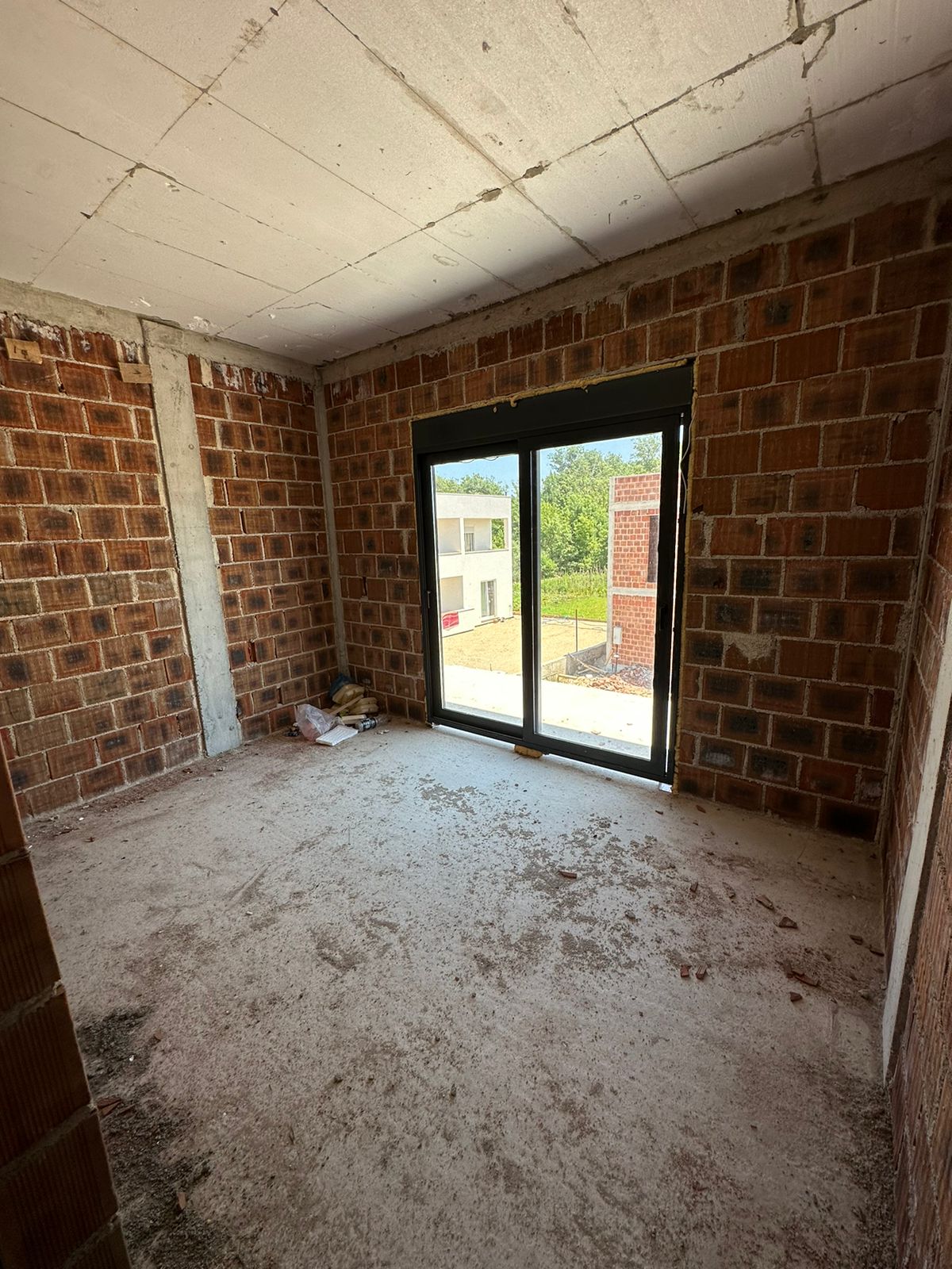 Unfinished room with brick walls, concrete ceiling, and wide glass doors overlooking Ulcinj&rsquo;s property market&mdash;exclusive by Ekosphere, immobilien.ekosphere.me.