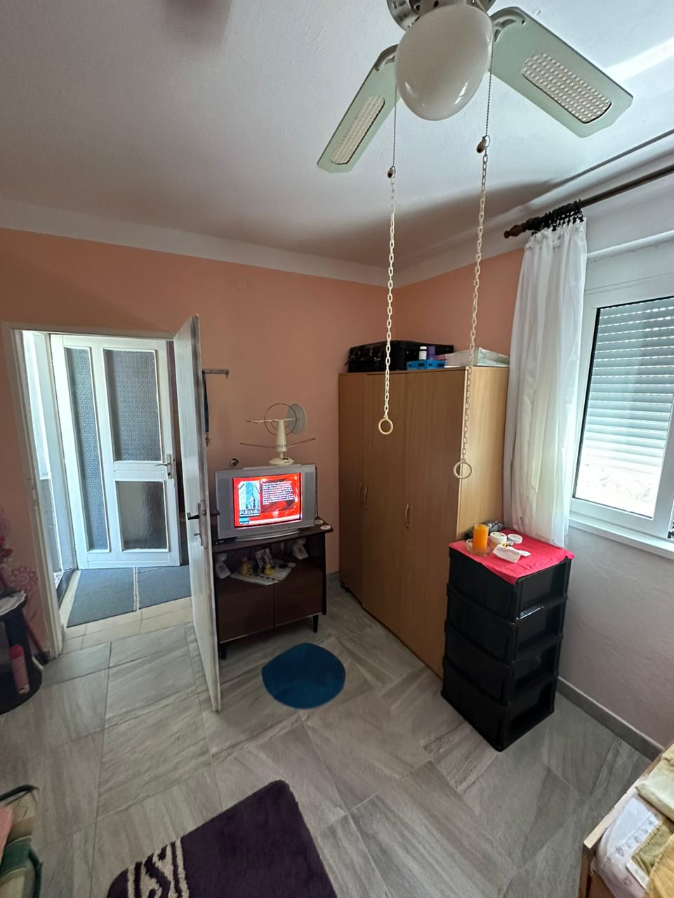 Modern Ulcinj room with tiled floors, ceiling fan, wardrobe, and TV. Prime real estate by Ekosphere DOO on immobilien.ekosphere.me.