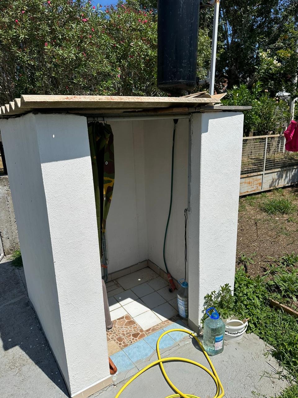 Modern outdoor shower with white walls, tiled floor, eco water tank&mdash;ideal Ulcinj property investment. By ekosphere doo on immobilien.ekosphere.me.
