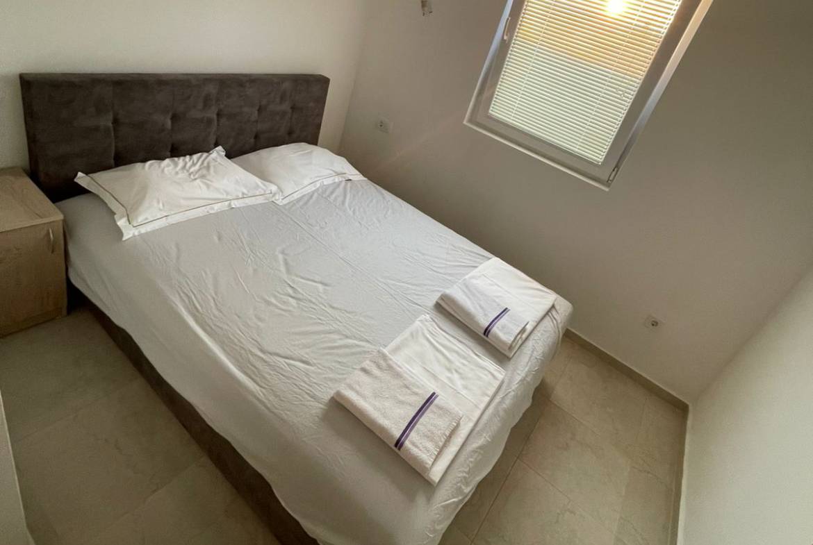 Modern Ulcinj bedroom with double bed, crisp linens, nightstand, window&mdash;prime real estate by ekosphere doo on immobilien.ekosphere.me.