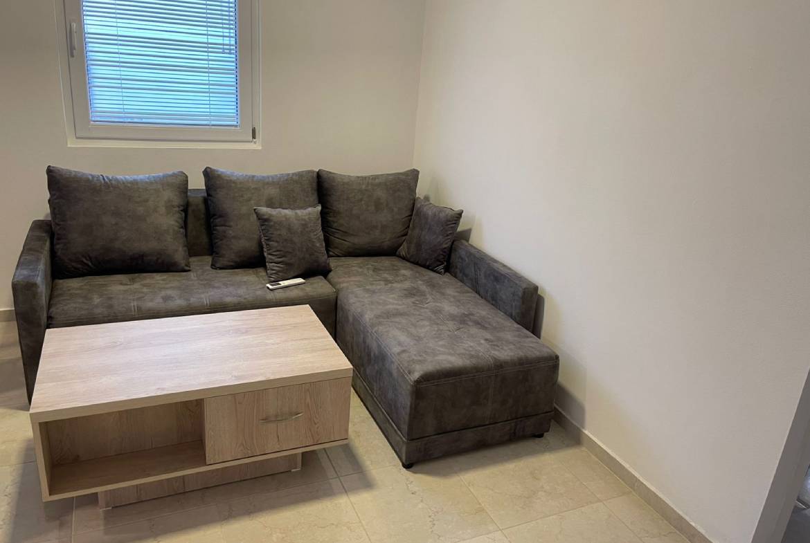 Modern Ekosphere home in Ulcinj: gray L-shaped sofa, wood coffee table, window blinds&mdash;exclusive at immobilien.ekosphere.me by Ekosphere doo.