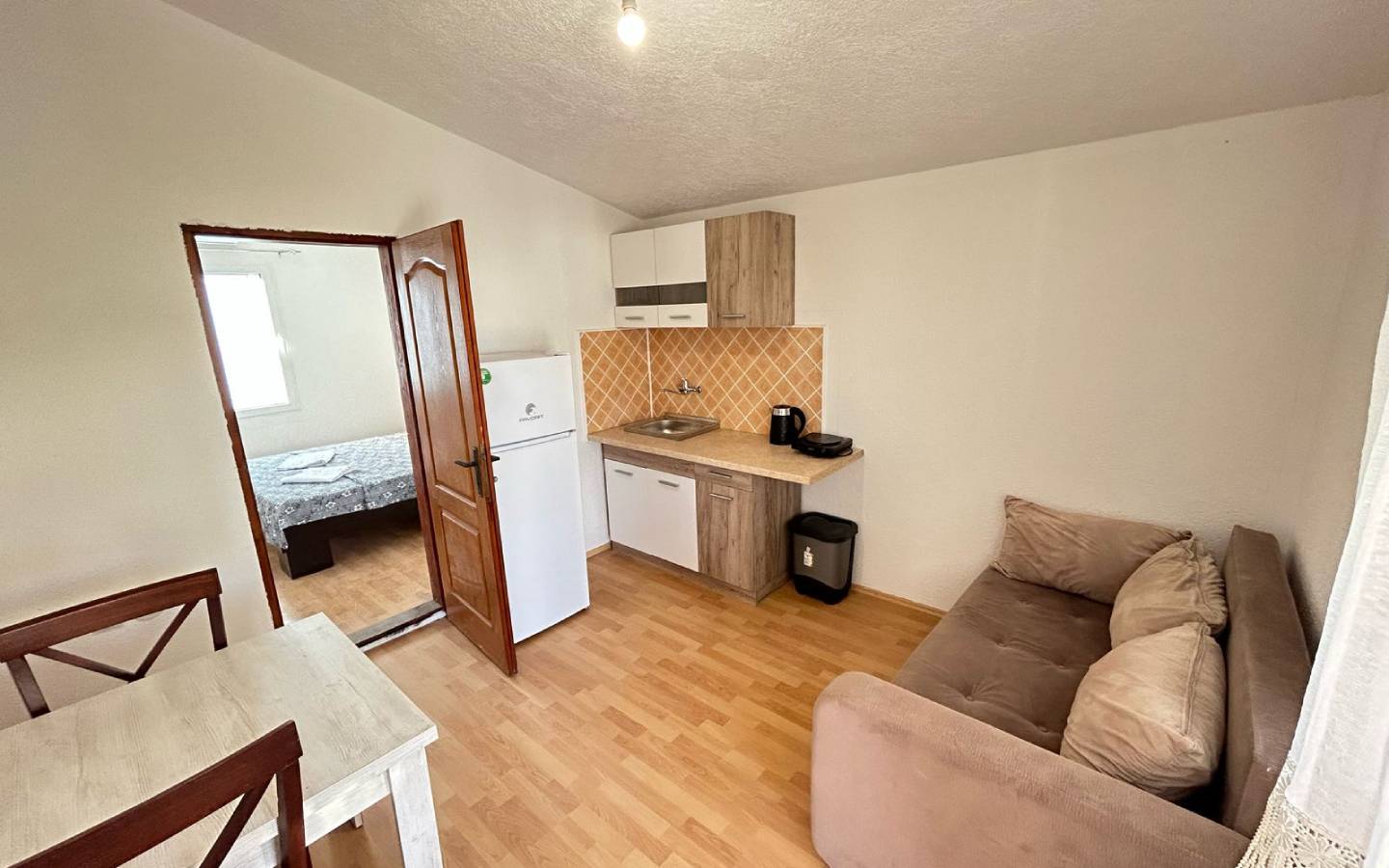 Modern Ulcinj apartment for sale: open kitchen, brown sofa, dining area, wood floors. Invest via immobilien.ekosphere.me by ekosphere doo.