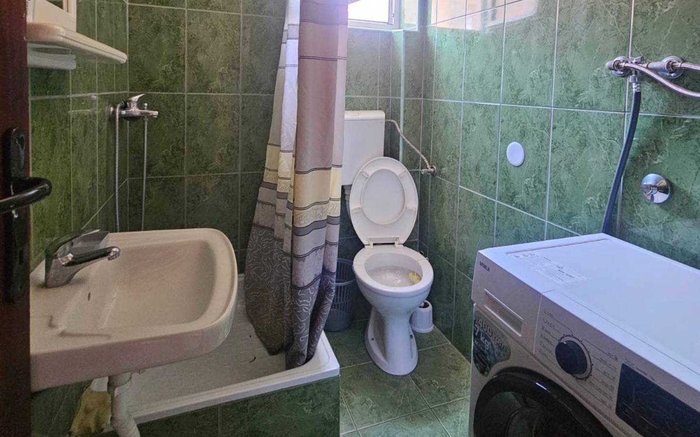 Modern green-tiled bathroom in Ulcinj with shower, washing machine, and natural light&mdash;prime real estate on immobilien.ekosphere.me by Ekosphere.