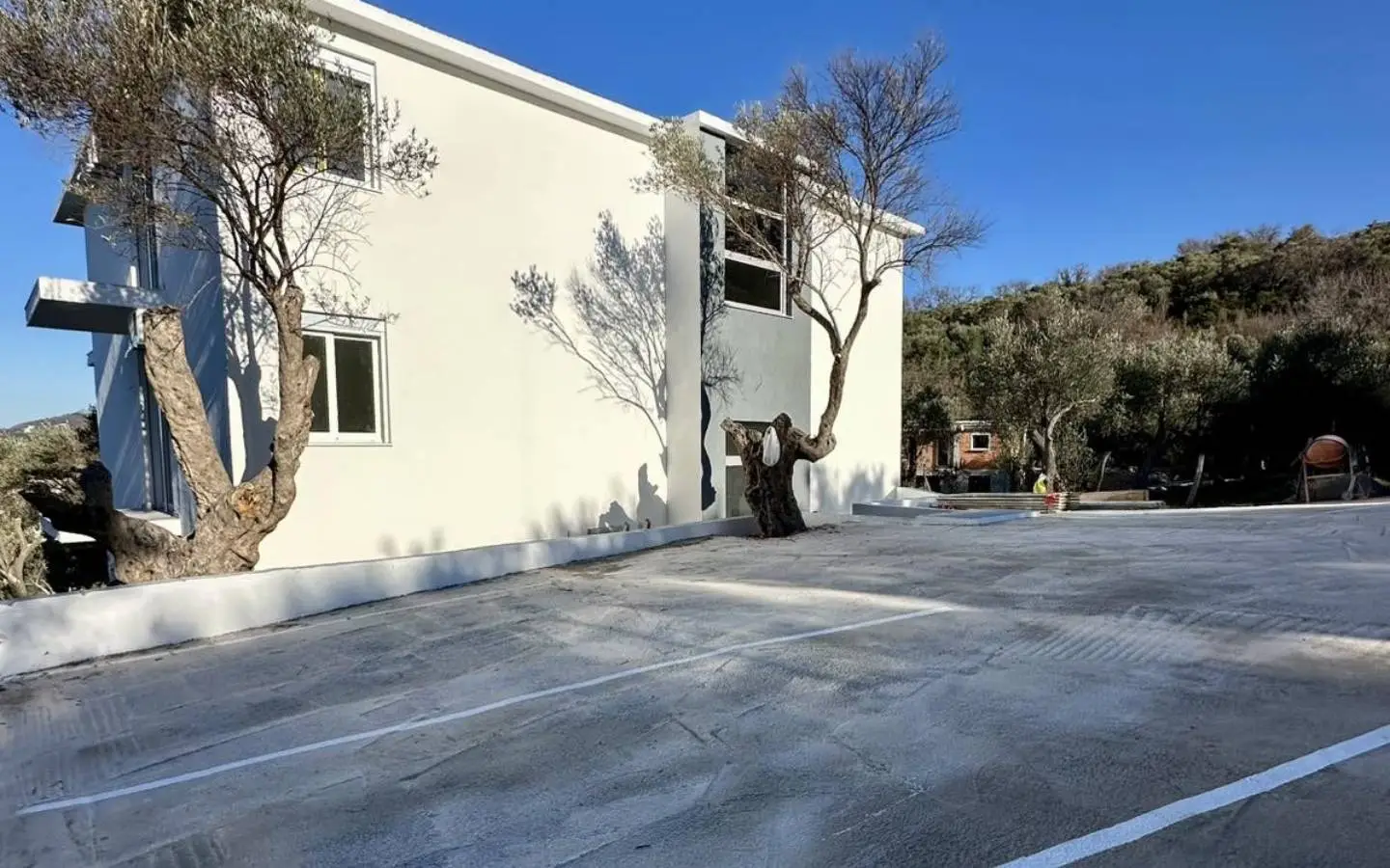 Modern white building with parking, lush greenery, and blue sky&acirc;prime Ulcinj real estate. Listed on immobilien.ekosphere.me by ekosphere doo.