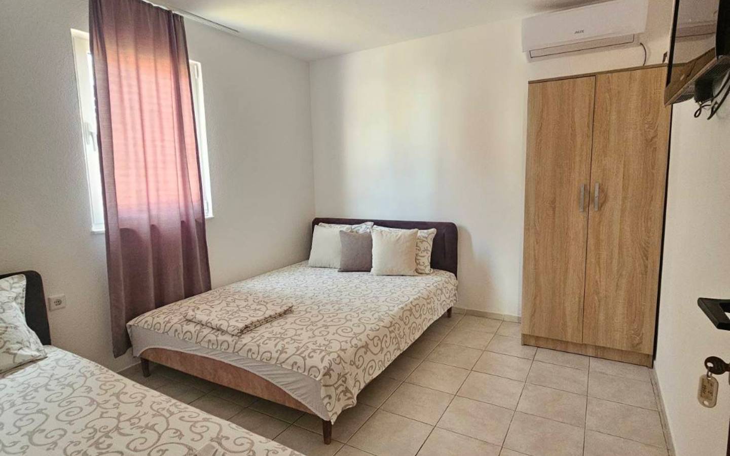 Modern Ulcinj bedroom with 2 beds, wardrobe, TV, window with pink curtains&mdash;prime real estate by Ekosphere on immobilien.ekosphere.me.