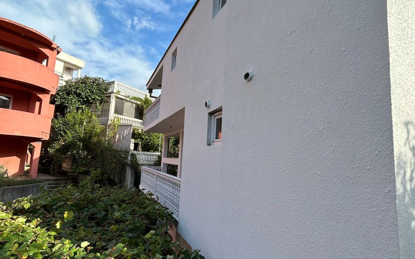 Modern white property in Ulcinj, Montenegro with balconies, security cameras, and lush greenery&mdash;exclusive on immobilien.ekosphere.me by Ekosphere doo.