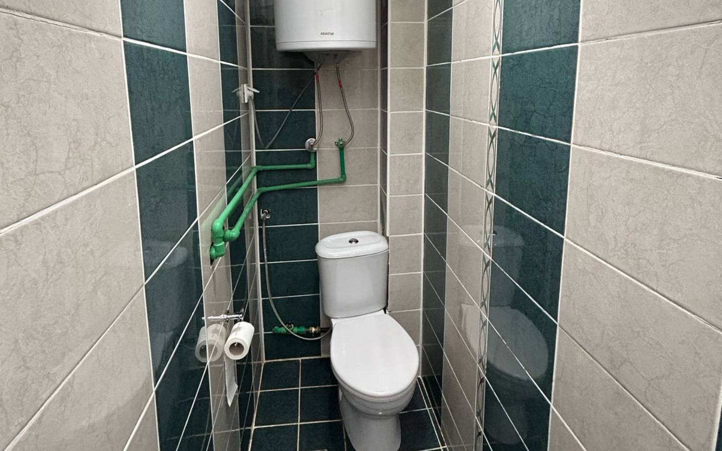 Modern narrow bathroom in Ulcinj property with tiled walls, white toilet, water heater; invest with immobilien.ekosphere.me by ekosphere doo.