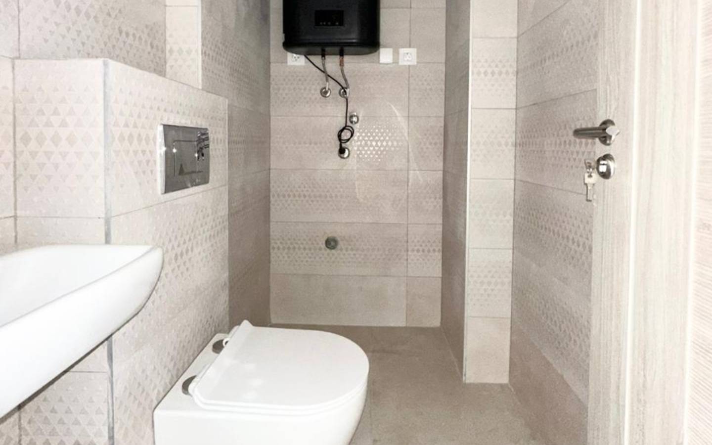 Modern tiled bathroom with wall-mounted toilet, corner sink, and water heater&mdash;ideal Ulcinj Montenegro investment. Montenegro-listings.me by Ekosphere.