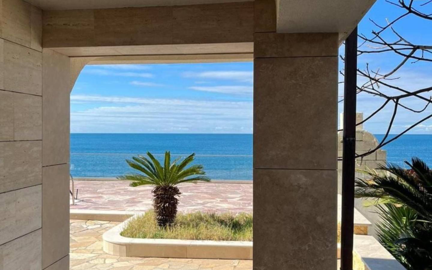 Stunning Ulcinj Montenegro property: ocean views through a stone arch, palm patio, by Ekosphere on immobilien.ekosphere.me.