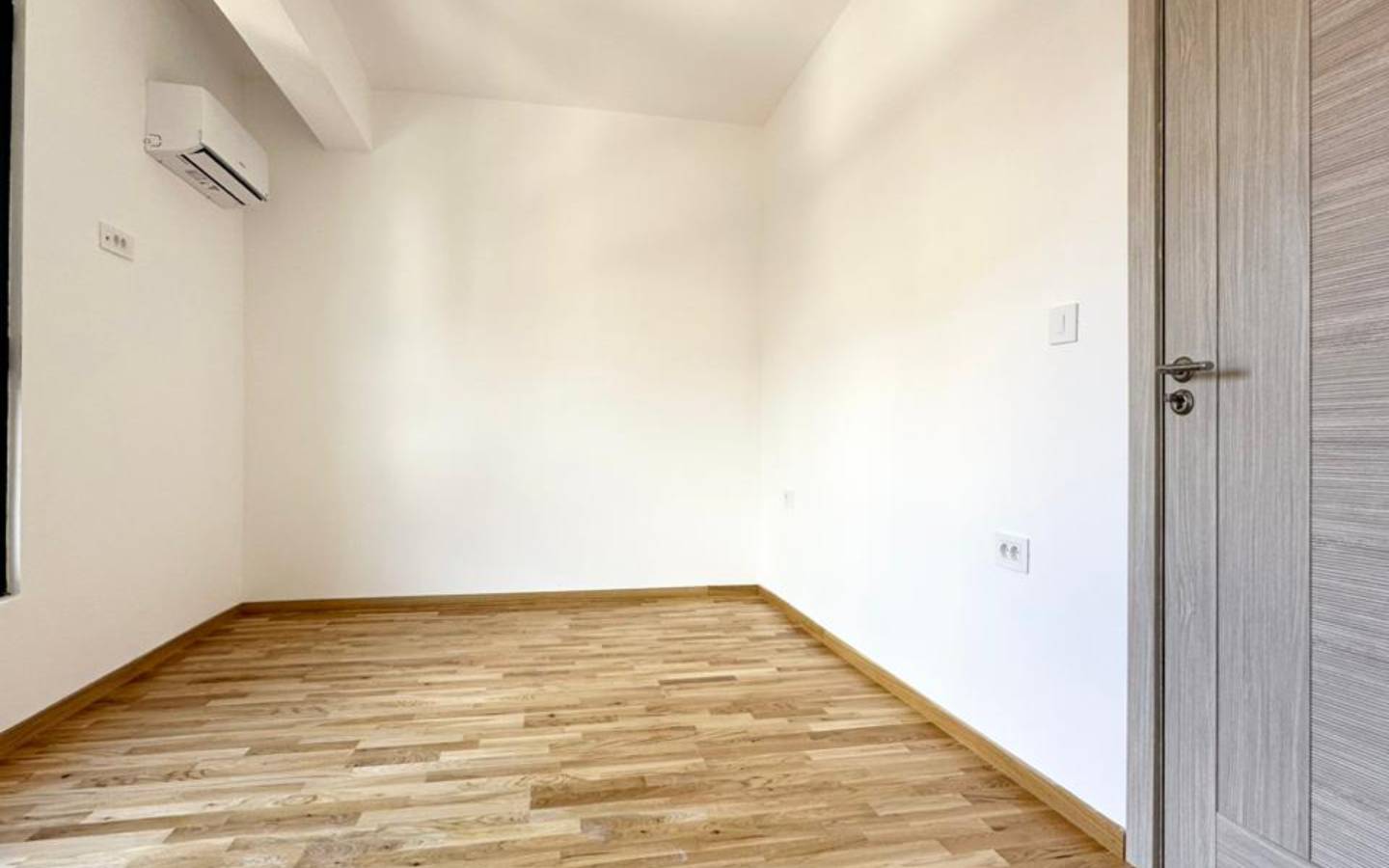 Modern, sunlit room with wooden flooring, white walls, AC, ideal Ulcinj investment. Listed on immobilien.ekosphere.me by Ekosphere.