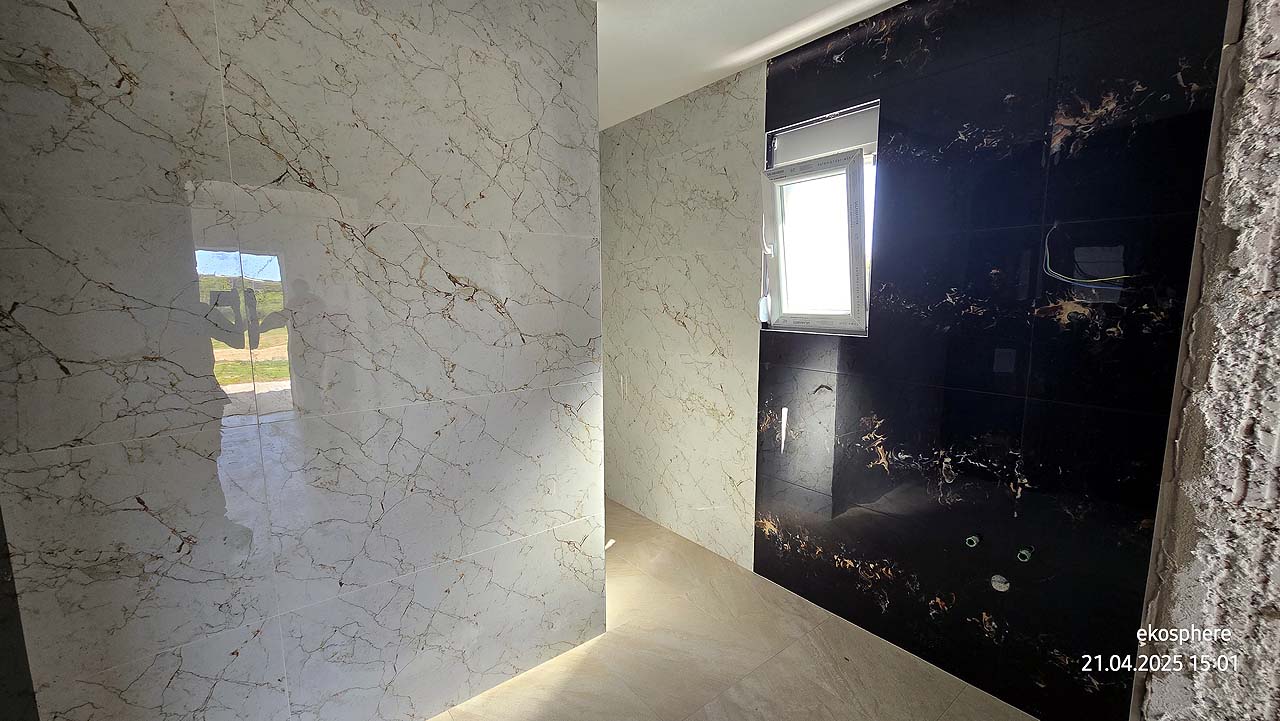 Modern bathroom in Ulcinj features marble tiles, black accent wall, natural light. Top Montenegro real estate by Ekosphere, on immobilien.ekosphere.me.