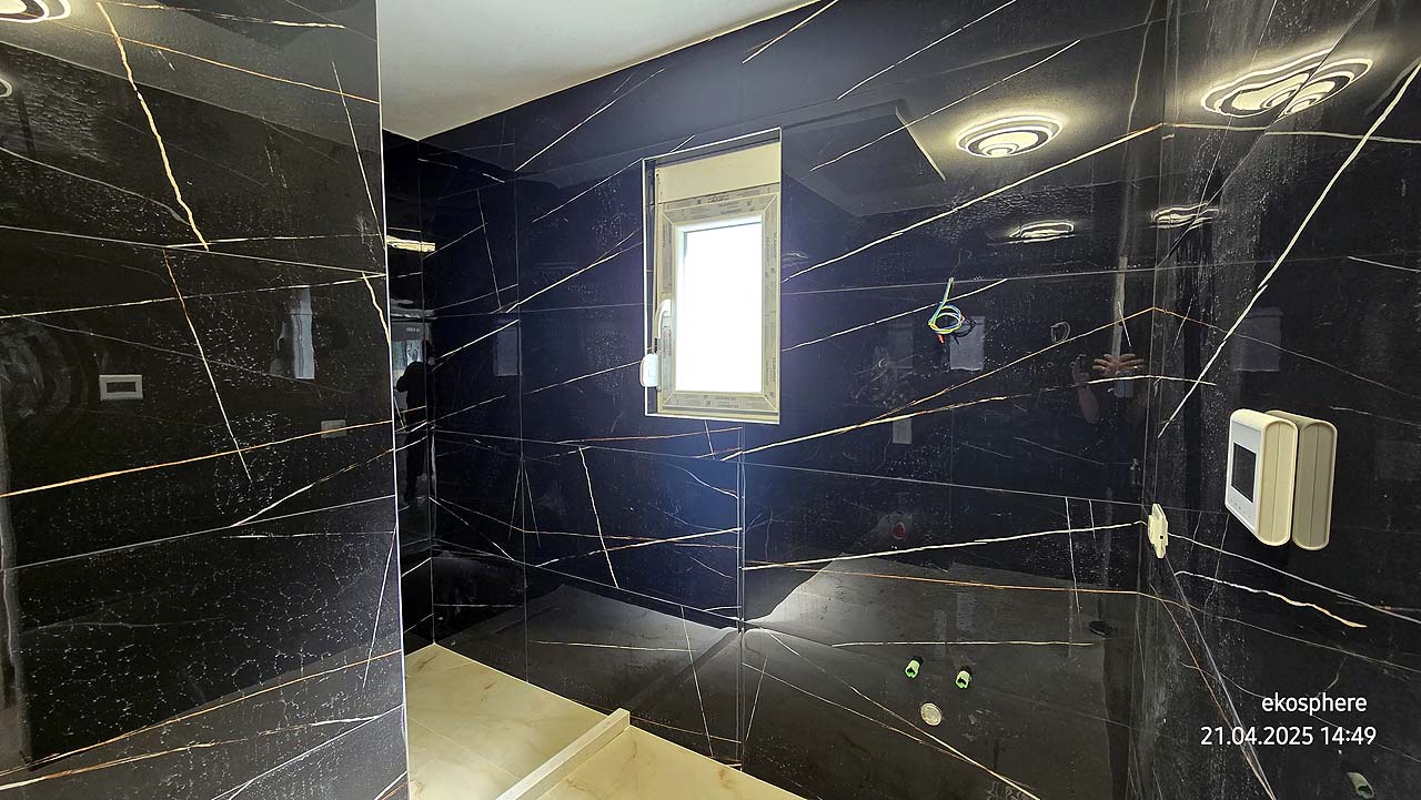 Modern Ulcinj bathroom with black marble walls, white fixtures, and natural light&mdash;exclusive at immobilien.ekosphere.me by Ekosphere.