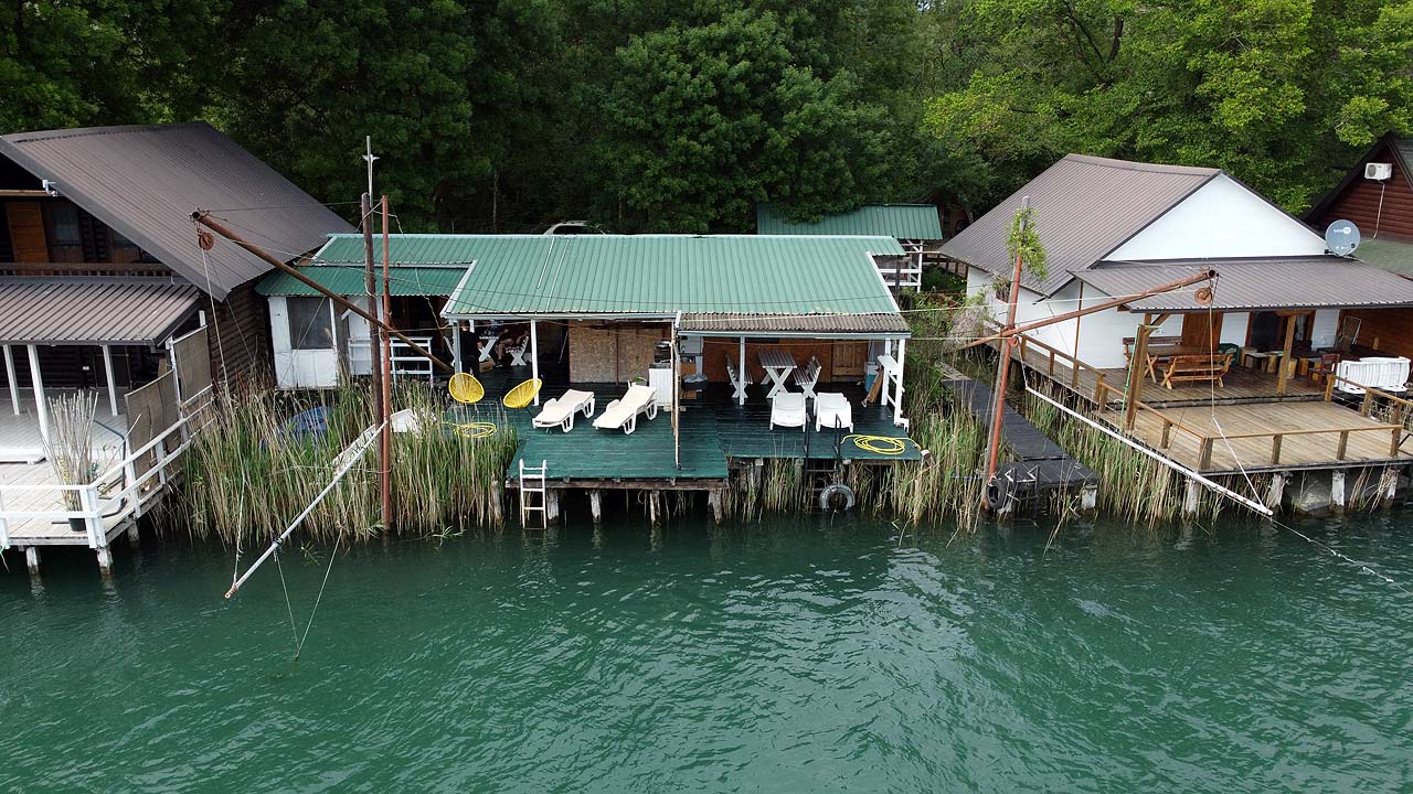 Stylish riverside deck with white seating, lush greenery, and eco-inspired buildings&mdash;premier Ulcinj real estate via ekosphere doo.