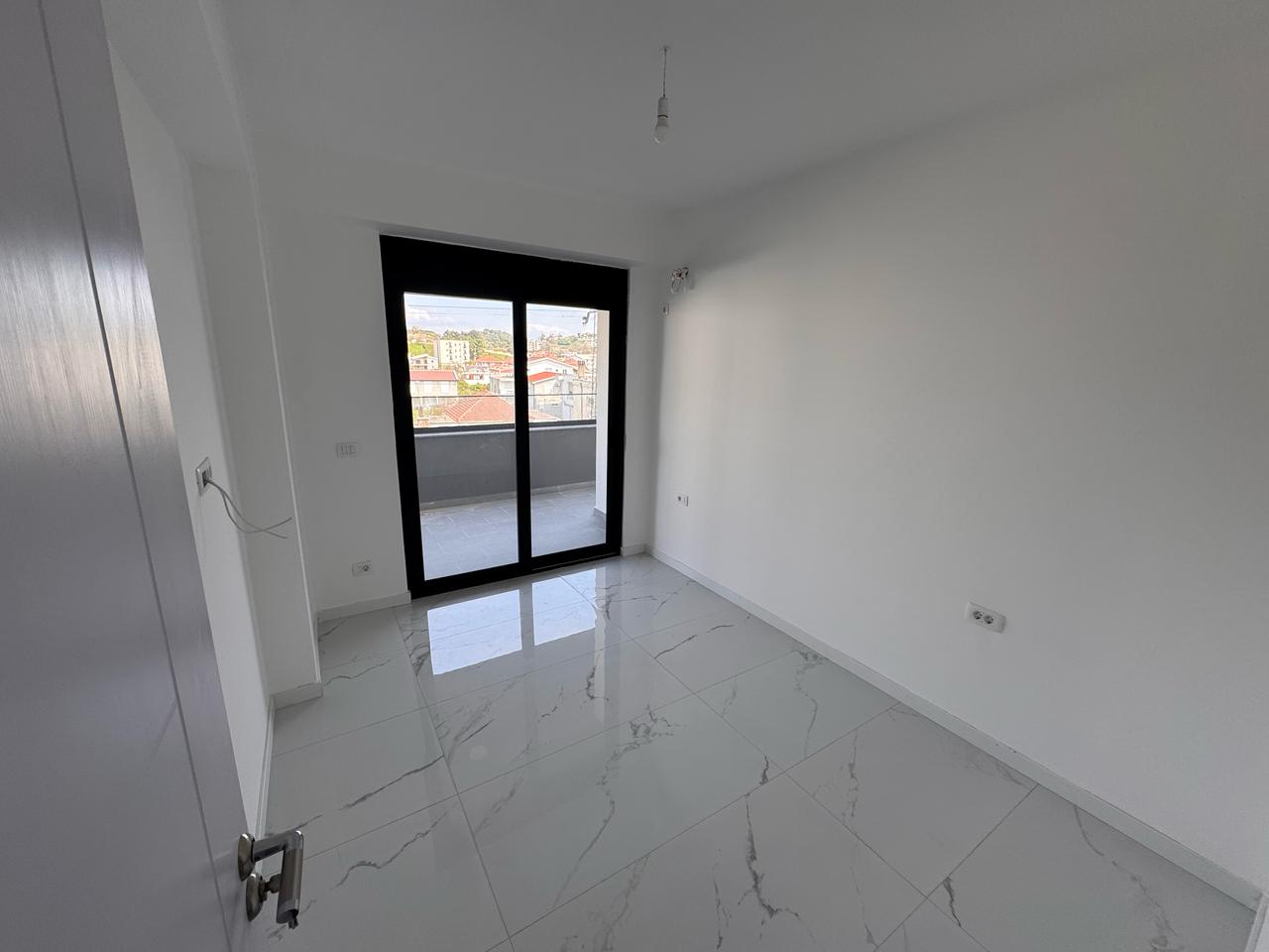 Bright, tiled room in prime Ulcinj real estate; large glass doors to balcony with city views. Exclusive on immobilien.ekosphere.me by Ekosphere doo.