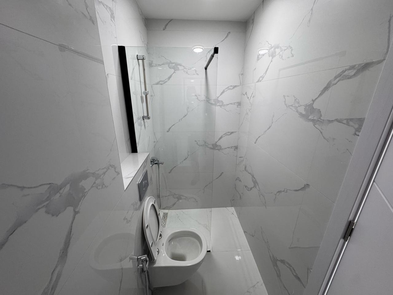 Modern bathroom in Ulcinj with marble tiles, wall-mounted toilet, glass partition&mdash;ideal investment at immobilien.ekosphere.me by ekosphere doo.