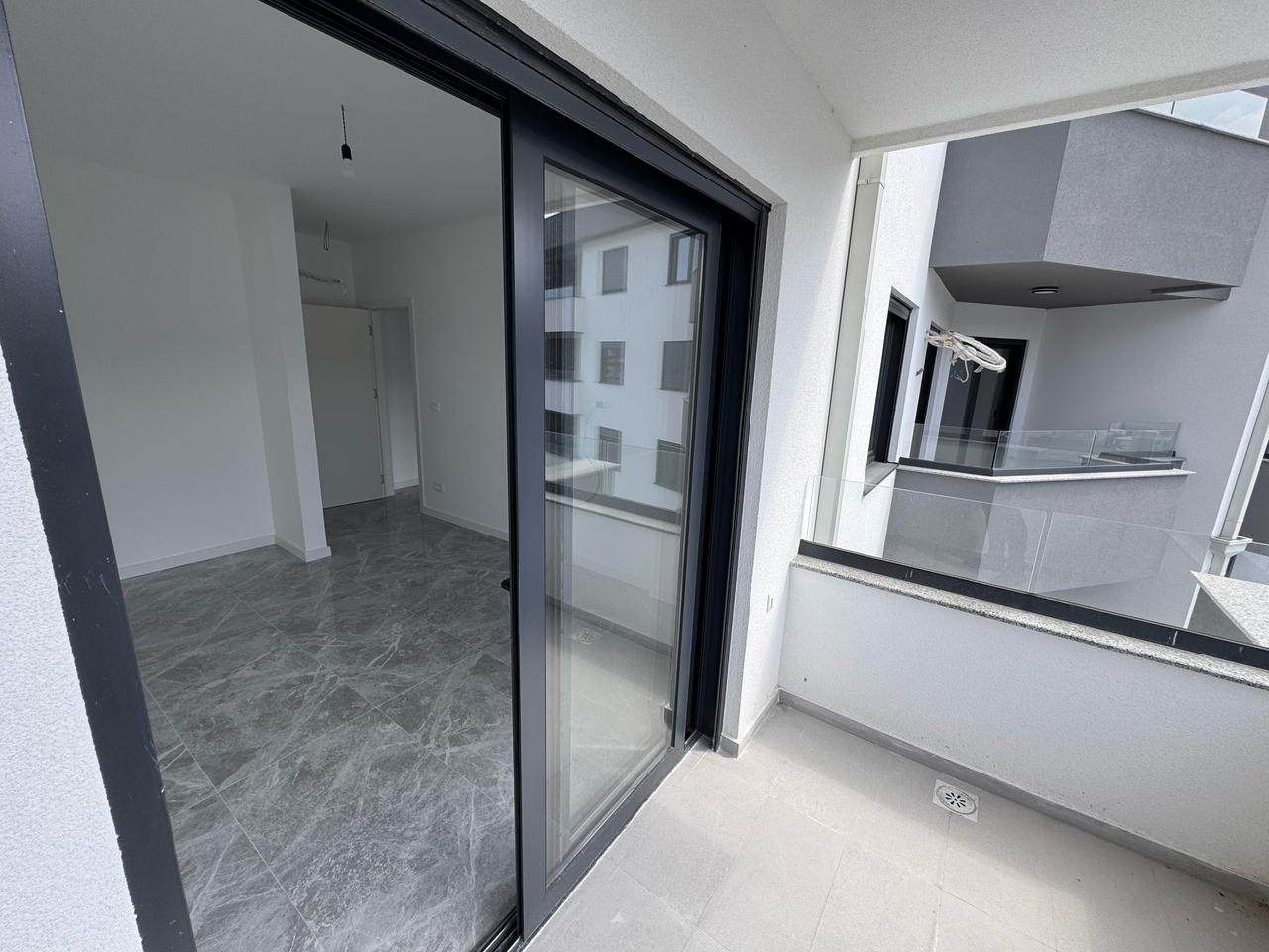 Modern covered balcony with light gray tiles; sliding doors open to airy, unfurnished interiors&mdash;prime Ulcinj real estate at immobilien.ekosphere.me by ekosphere doo.