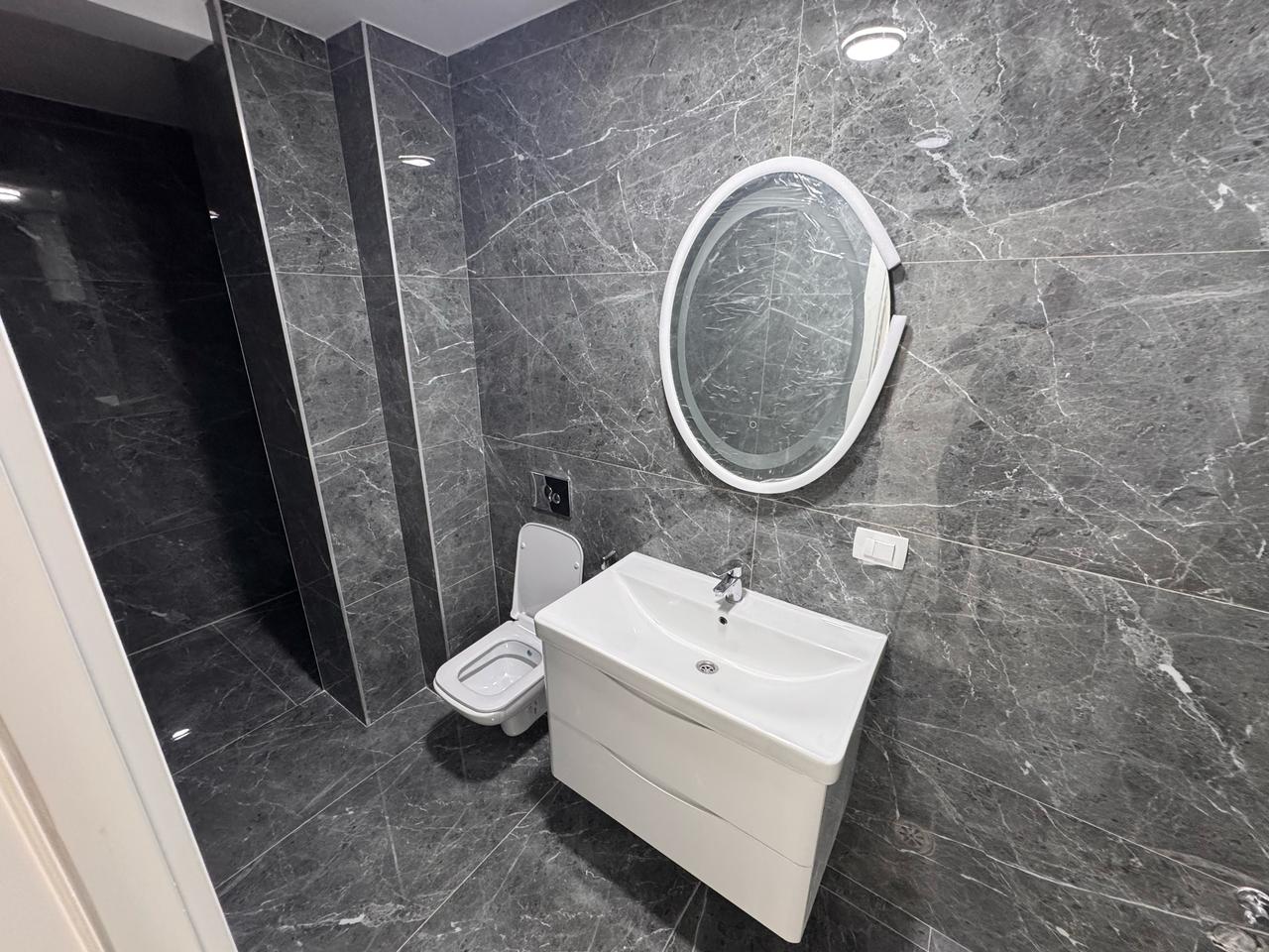 Luxurious modern bathroom with dark marble, wall-mounted toilet, elegant vanity and mirror in Ulcinj&mdash;featured on immobilien.ekosphere.me.