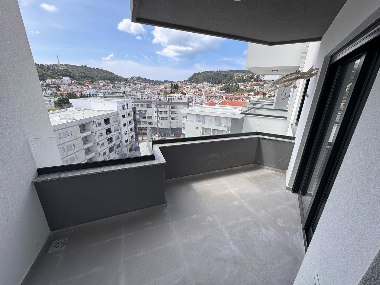 Luxury modern apartment balcony with tiled floors and glass railing, offering stunning Ulcinj city views&mdash;exclusive at immobilien.ekosphere.me by Ekosphere doo.