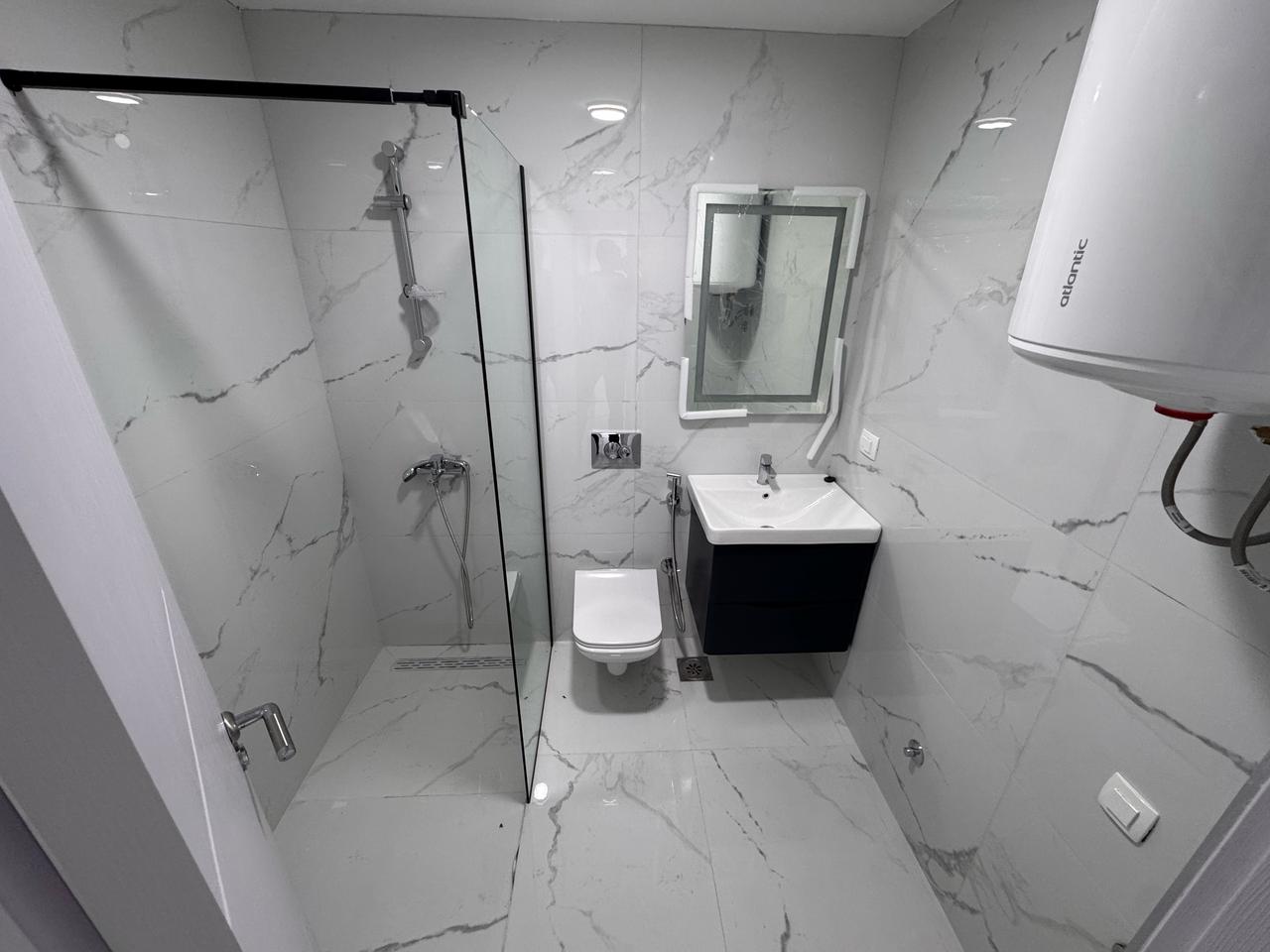 Sleek Ulcinj bathroom with gray marble, wall-mounted toilet, floating sink, glass shower&mdash;exclusive at immobilien.ekosphere.me by Ekosphere.