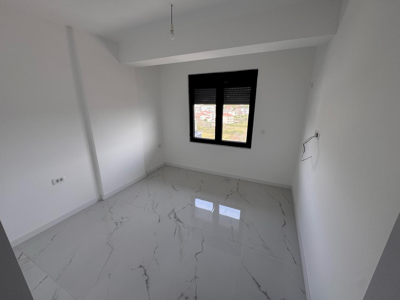 Modern minimalist room in Ulcinj with white walls, elegant tile floors, and a black-framed window. Offered by immobilien.ekosphere.me.
