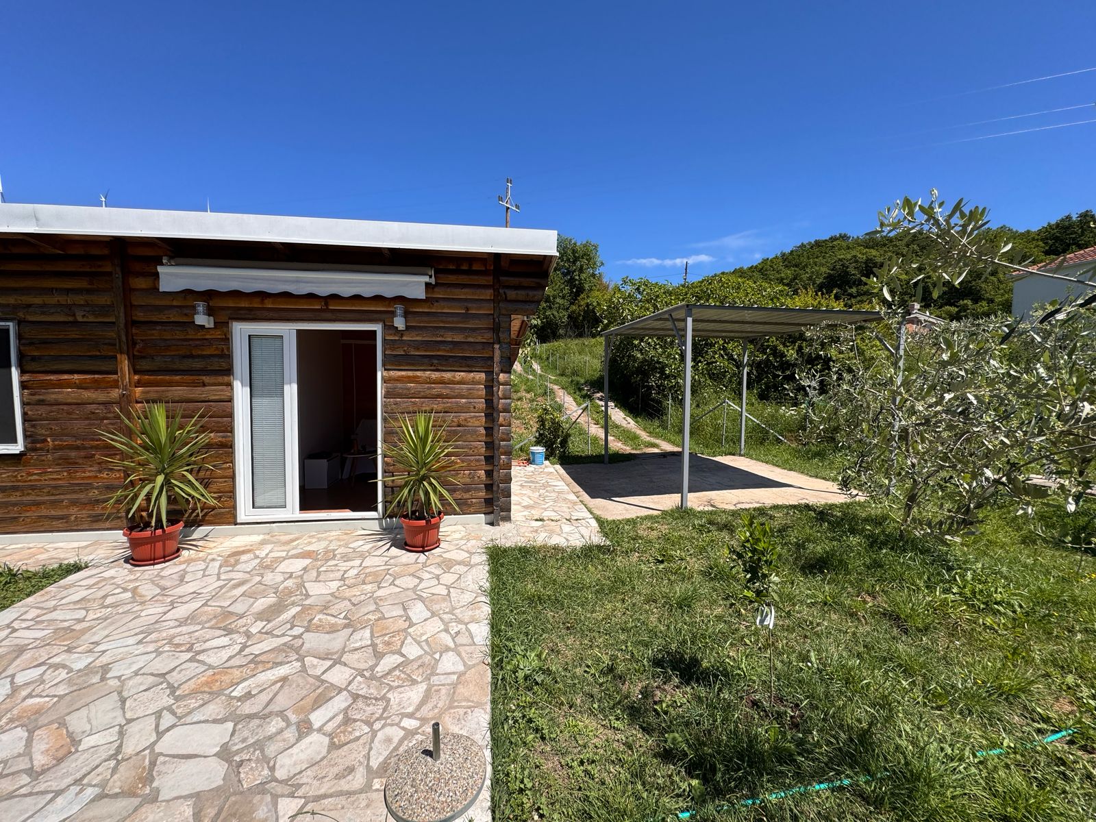 Charming wooden home with stone patio, carport, and lush lawn in Ulcinj. Invest via immobilien.ekosphere.me by ekosphere doo.