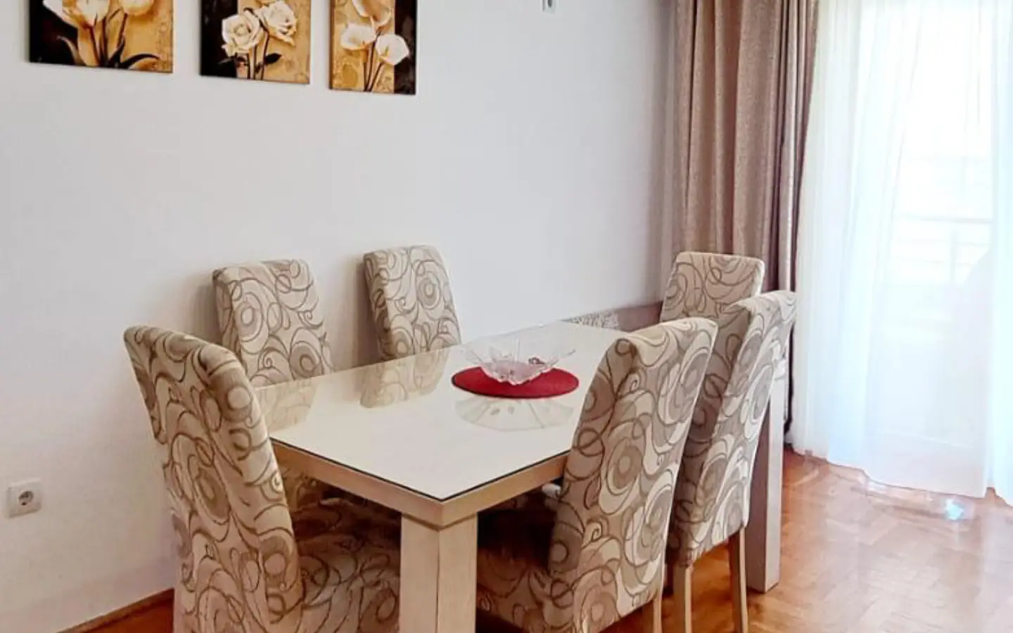Elegant Ulcinj Montenegro property dining area with glass-top table, designer chairs, sheer curtains, floral art. Eksphere doo project.