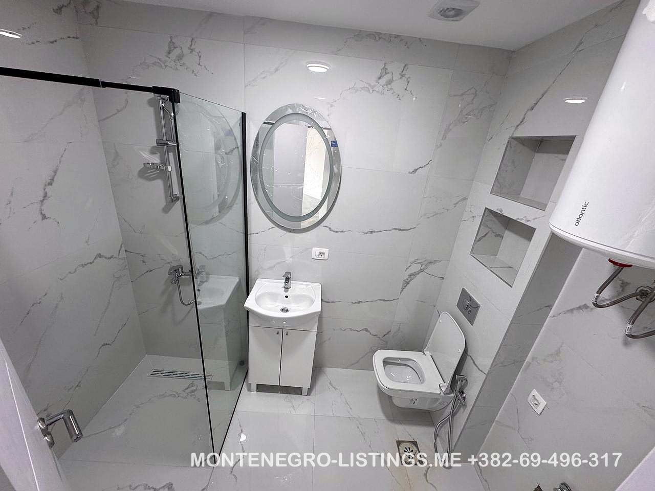 Elegant Ulcinj bathroom with marble tiles, glass shower, modern fixtures. Great real estate investment at immobilien.ekosphere.me by Ekosphere.