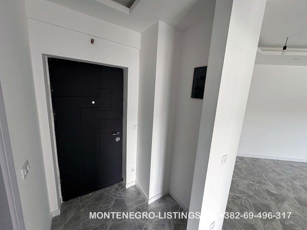Contemporary Ulcinj apartment entry: sleek black door, white walls, grey tiled floor. Invest with immobilien.ekosphere.me by ekosphere doo.