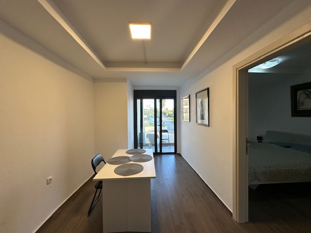Modern minimalist dining area with sleek white table, balcony access, quality wood floors&mdash;ideal Ulcinj real estate at immobilien.ekosphere.me (a project of ekosphere doo).