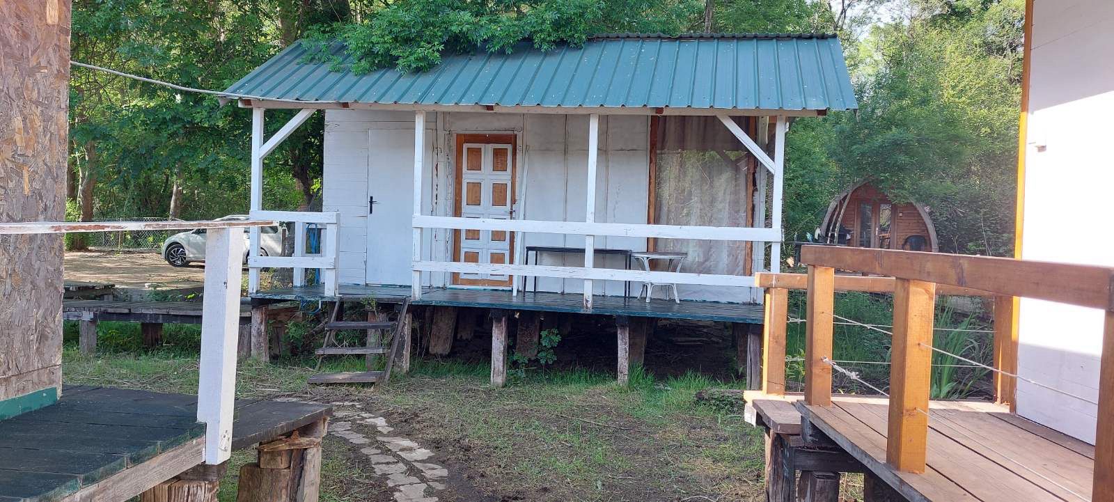 Charming white wooden cabin on stilts with green metal roof, porch, and parking in Ulcinj&mdash;prime real estate by immobilien.ekosphere.me.