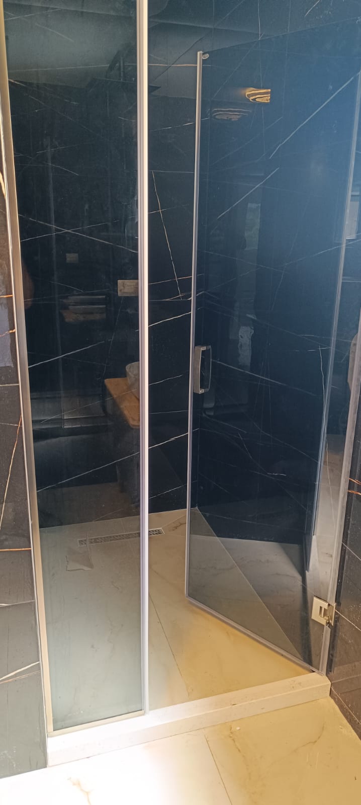 Luxurious shower with marble-patterned tiles, glass panels, and wood accents&mdash;exclusive property in Ulcinj by ekosphere doo on immobilien.ekosphere.me.
