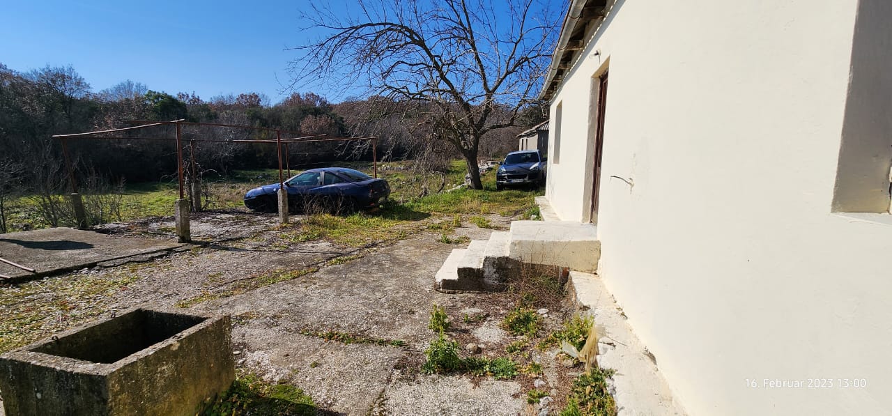 Bright concrete yard next to a pale building with steps, cars, and hills&mdash;prime Ulcinj real estate on immobilien.ekosphere.me by ekosphere doo.
