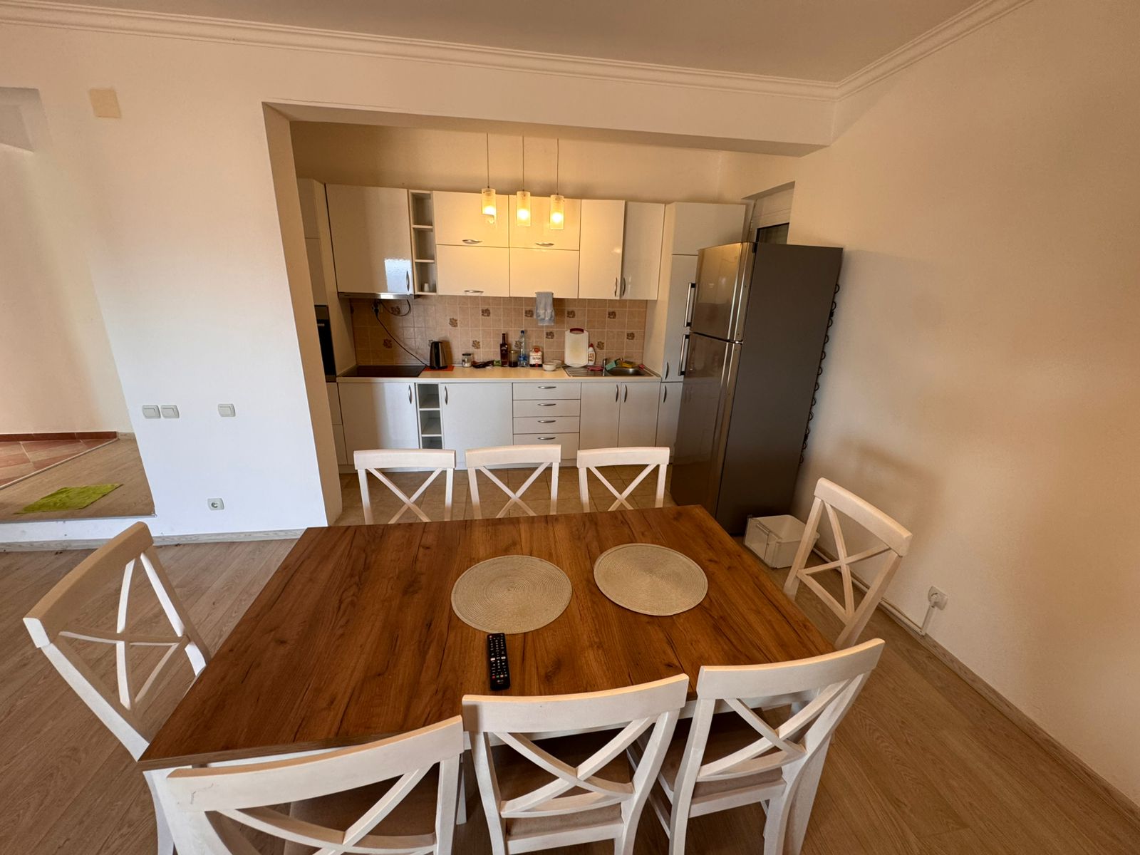 Modern Ulcinj kitchen with white cabinets, stainless fridge, wood table; ideal real estate on immobilien.ekosphere.me by ekosphere doo.