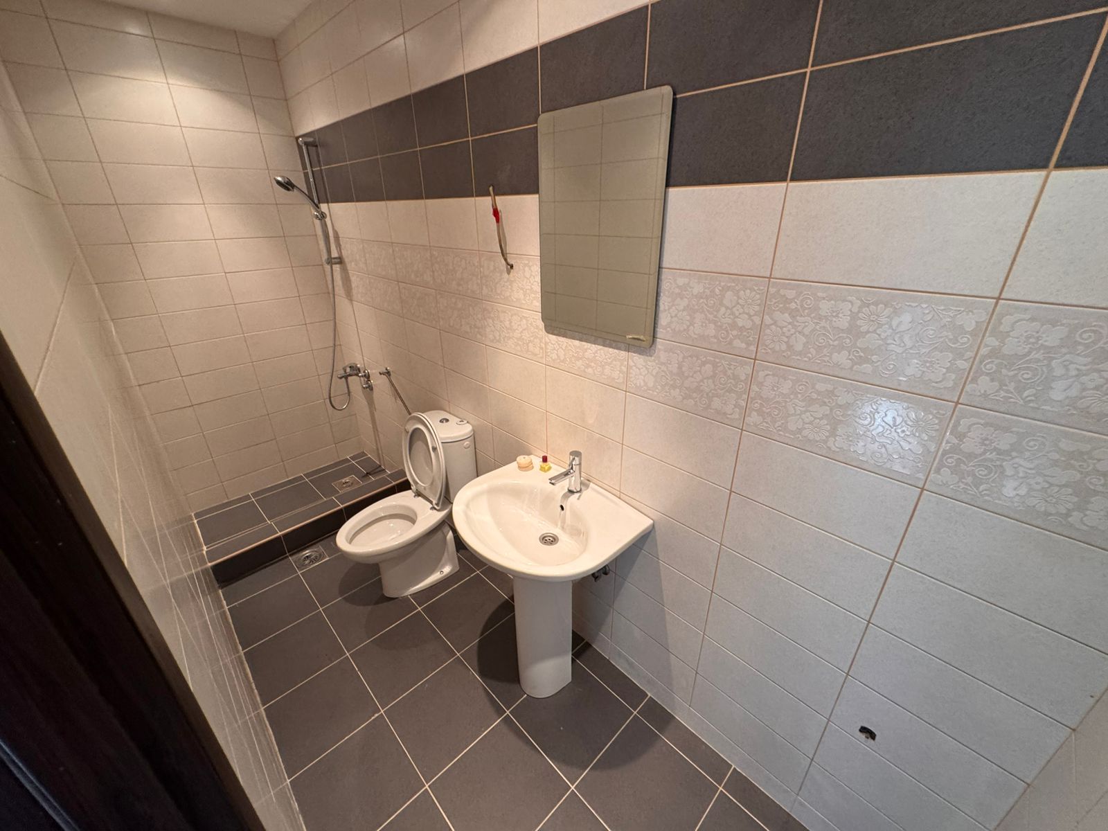 Modern Ulcinj Montenegro property bathroom: tiled in gray and white, with shower, sink, and mirror. Discover more on immobilien.ekosphere.me by ekosphere doo.