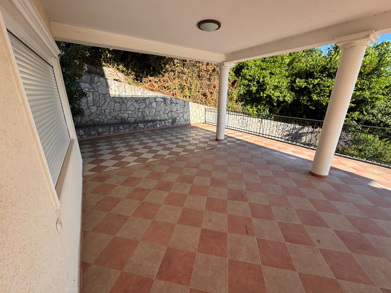 Elegant covered patio in Ulcinj, Montenegro with checkered tile, white columns, and lush greenery. Exclusive by immobilien.ekosphere.me (Ekosphere).