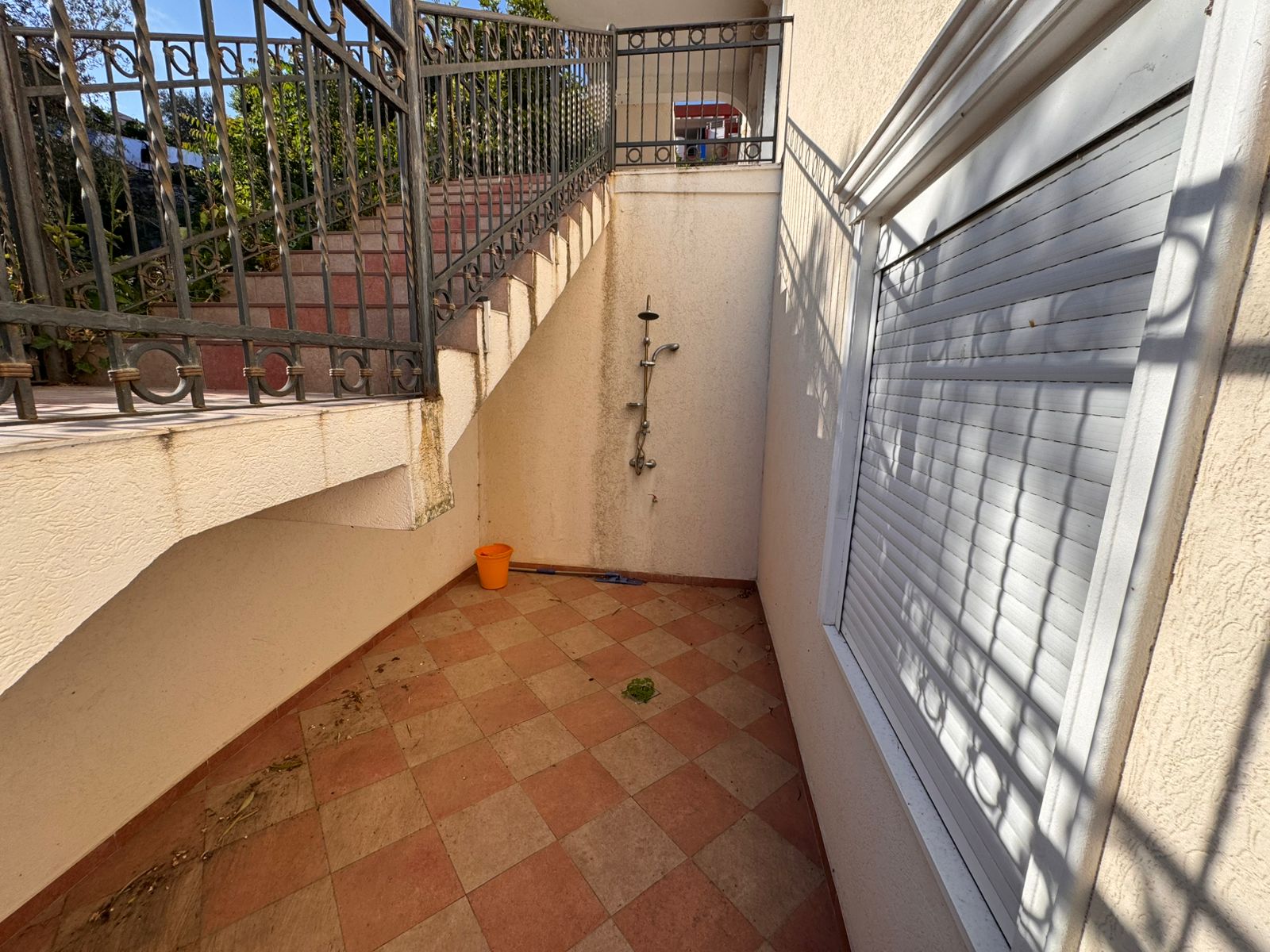 Stylish outdoor tiled space under stairs with modern shower, railings, and shuttered window&mdash;prime Ulcinj real estate by Montenegro-listings.me, a project of Ekosphere doo.