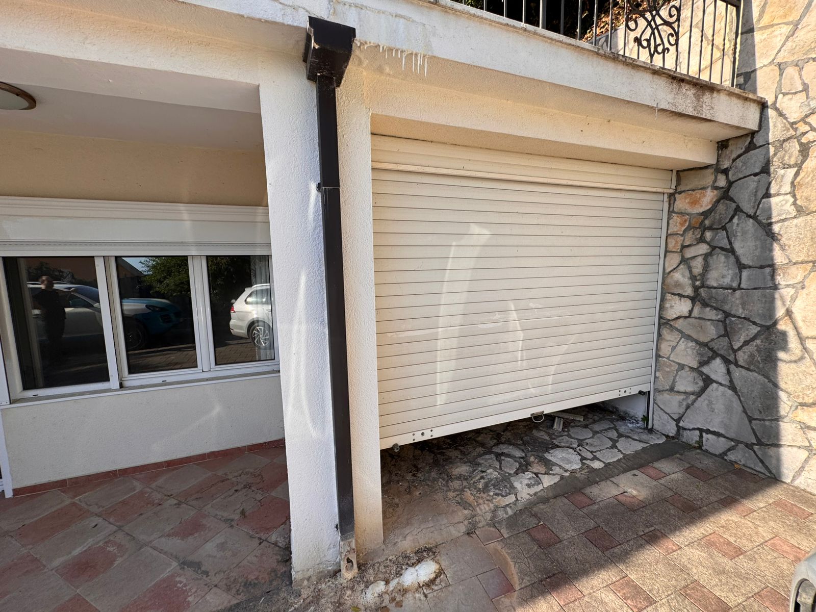 Modern stone and concrete garage with white roll-up door, tiled drive, and reflective windows&mdash;prime Ulcinj real estate by ekosphere doo.