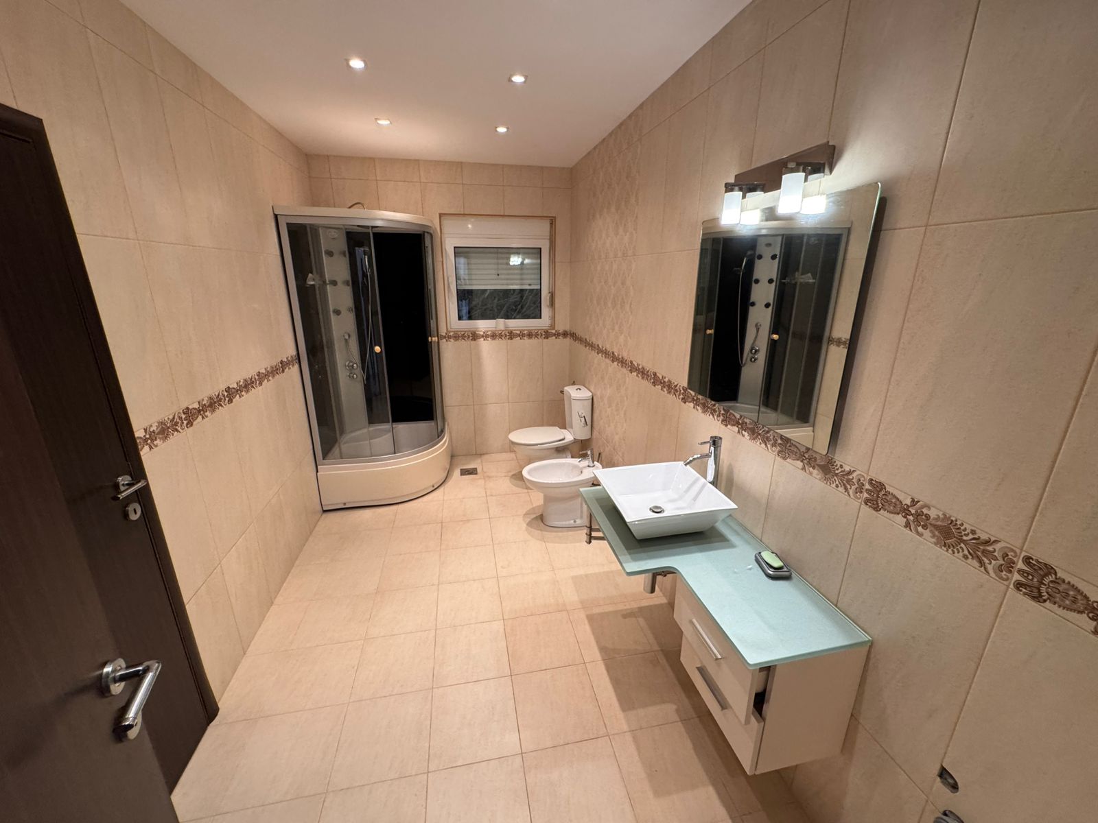 Elegant Ulcinj bathroom: beige tiles, glass shower, premium fixtures&mdash;ideal property investment on immobilien.ekosphere.me by ekosphere doo.