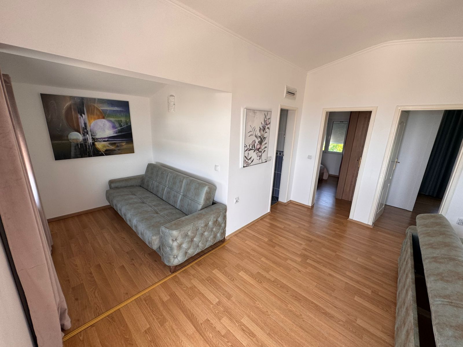 Modern Ulcinj property with light wood floors, sleek gray sofa, wall art, and open layout. Listed by immobilien.ekosphere.me, Ekosphere doo.